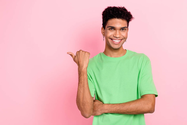 Photo of cheerful positive guy wear green t-shirt pointing thumb empty space isolated pink color background. - Фото, изображение