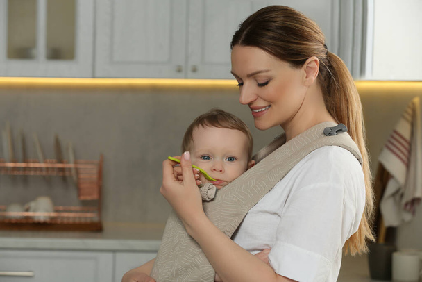 Mother feeding her cute child in sling (baby carrier) at home - Photo, Image