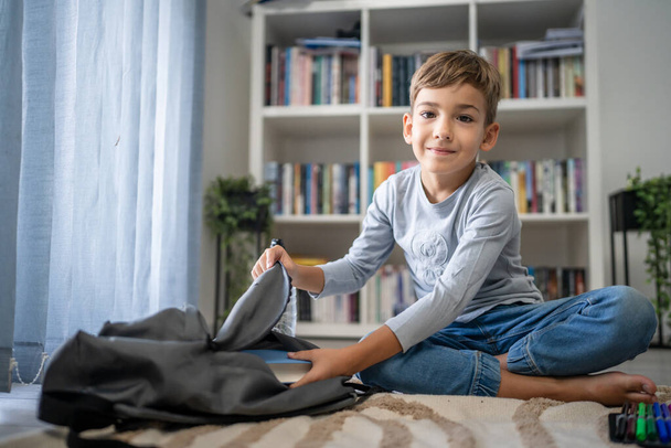 Маленький мальчик кавказский ученик ребенка подготовить свой рюкзак для первого дня школы обратно в школу и концепция образования сидеть на полу дома упаковывать свои вещи реальные люди копировать пространство - Фото, изображение
