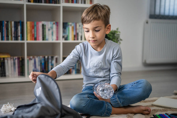 Small caucasian boy pupil child prepare his backpack for first day of school back to school and education concept sit on the floor at home packing his stuff real people copy space - Photo, Image