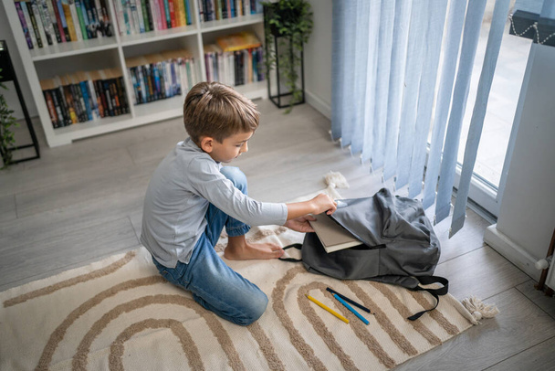 Small caucasian boy pupil child prepare his backpack for first day of school back to school and education concept sit on the floor at home packing his stuff real people copy space - Photo, Image