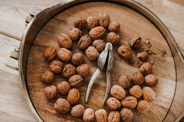 Walnuts Abundance and metal nutcracker in a bowl on a wooden table. Healthy food and snacks.Healthy fats. Keto diet ingredient. Nuts and seeds. Useful healthy snack. - Photo, Image