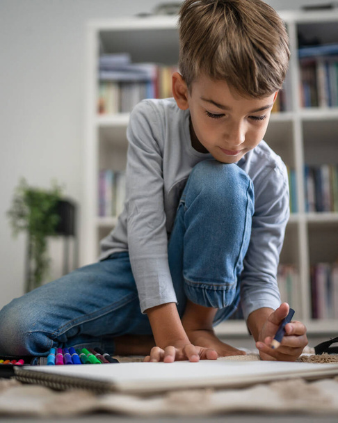 ένα σχολιαρόπαιδο Μικρό καυκάσιο αγόρι παίζει στο σπίτι Ισοπαλία στο πάτωμα κάνει την ανάπτυξη της παιδικής ηλικίας στο σπίτι μεγαλώνοντας και την εκπαίδευση έννοια αντιγραφή χώρο της οικιακής ζωής - Φωτογραφία, εικόνα
