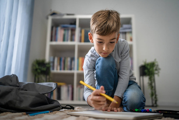 een schooljongen Kleine blanke jongen spelen thuis trekken op de vloer doen huiswerk kindertijd ontwikkeling opgroeien en onderwijs concept kopiëren ruimte huishoudelijk leven - Foto, afbeelding