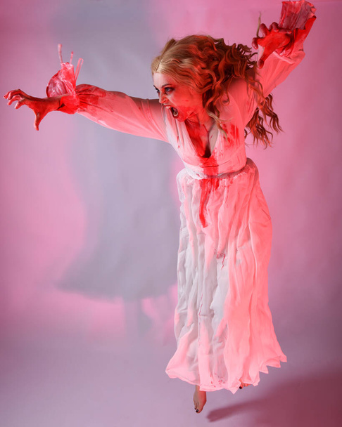 Retrato de comprimento total vampiro assustador noiva zumbi vestindo vestido de fantasia de Halloween sangrento. Os braços gestuais de pose de salto dinâmico estendem-se. Estúdio isolado com iluminação vermelha cinematográfica. - Foto, Imagem