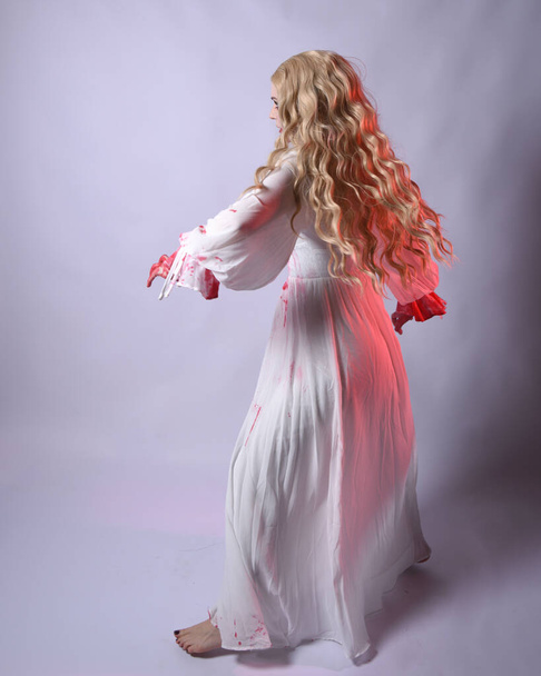  Pełna długość portret przerażającej wampirzej panny młodej zombie, noszenie eleganckiej sukienki halloween fantasy kostium z krwawą czerwoną farbą rozbryzgi. Stoję w pozycji. Izolacja na białym tle studia  - Zdjęcie, obraz