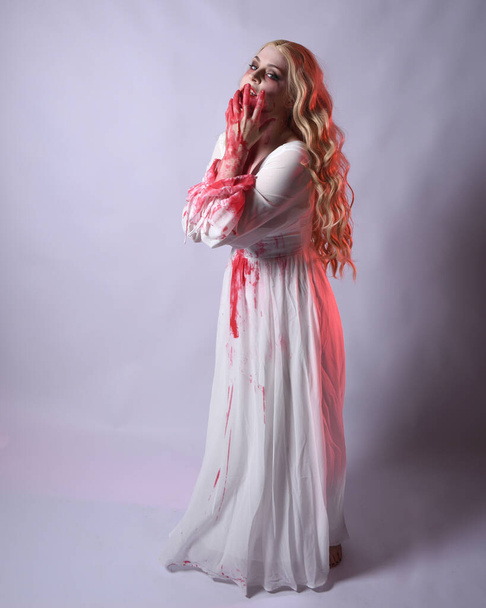  Plně dlouhý portrét strašidelné upíří zombie nevěsty, oblečené v elegantních halloweenských kostýmech s krvavými červenými skvrnami. stojící póza. Izolováno na bílém pozadí studia  - Fotografie, Obrázek