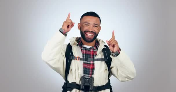 Hiking, travel and face of man in studio pointing up, dance and freedom celebration on grey background. Adventure, portrait and male backpacker dancing for news, announcement or explore opportunity. - Footage, Video