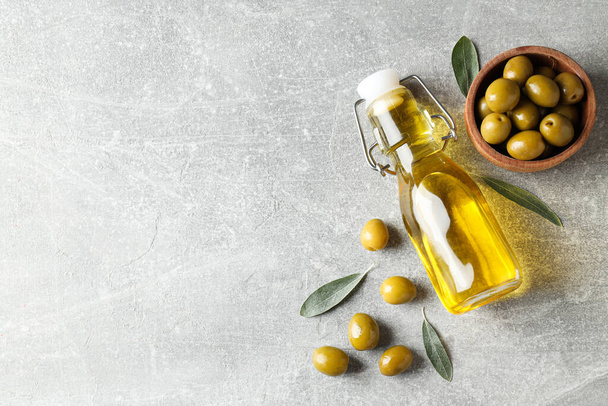 Пляшка оливкової олії та оливок на сірому фоні, простір для тексту - Фото, зображення