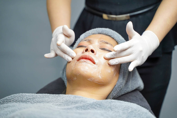 Cosmetólogo de primer plano aplicando crema suave mascarilla facial blanca y masaje en la mujer de belleza haciendo spa facial en clínica de belleza. - Foto, imagen
