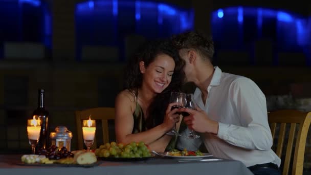 Gelukkige man en vrouw toasten en drinken wijn, terwijl de man fluistert iets in het vrouwelijke oor. Romantisch afspraakje op het dak. Romantisch concept. Een paar verliefd. Real time - Video