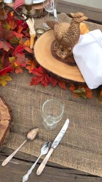 Auf dem Tisch stehen Teller auf Holzständern neben Gabeln Messer und Gläser Trockene Köpfe roter und schwarzer maisroter Servietten in der Mitte alles bereit für das Abendessen an Halloween Herbst Oktober Abend  - Filmmaterial, Video