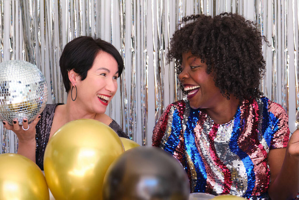 Twee vrienden die lachen op een feestje. Multiraciale vrouwen in een feest met ballonnen. - Foto, afbeelding