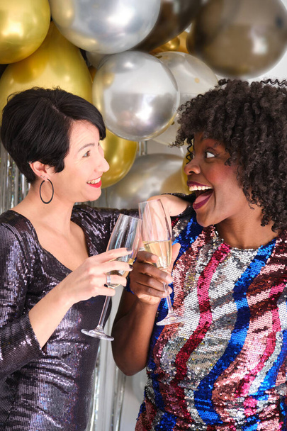 Δύο γυναίκες με ποτήρια σαμπάνιας που κάνουν πρόποση και γιορτάζουν την Πρωτοχρονιά σε ένα πρωτοχρονιάτικο πάρτι. - Φωτογραφία, εικόνα