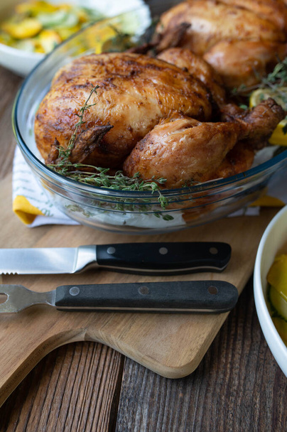 Pečené kuře ve skleněném kastrolu s citrónem a tymiánem na dřevěném stole. - Fotografie, Obrázek