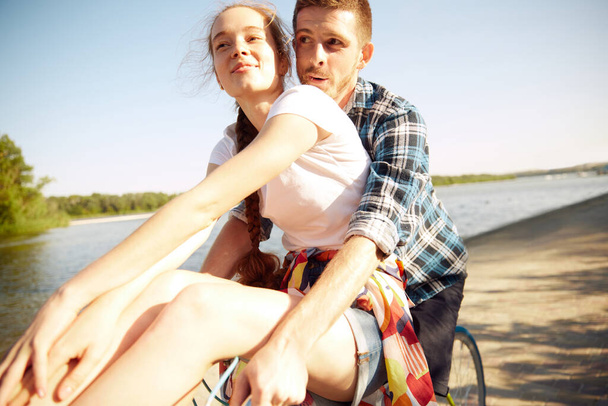 若い陽気で素敵なカップルの肖像画は,夜の暑い夏の日に川のエンバンクを乗り越えて楽しいサイクルに乗っています. ロマンチックな関係,休暇,アクティブなライフスタイルのコンセプト. - 写真・画像