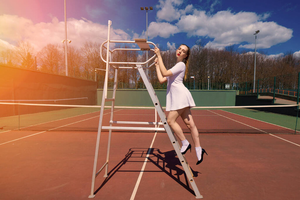 Seksikäs tyttö tennispelaaja valkoinen mekko ja korkokengät tilalla tennismaila kentällä. Nuori nainen pelaa tennistä, urheilu - Valokuva, kuva