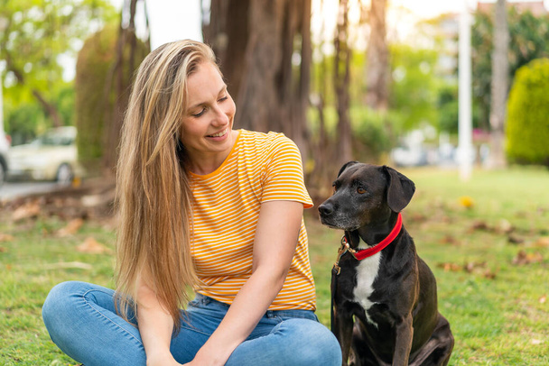 Jeune femme blonde avec son adorable chien noir à l'extérieur - Photo, image