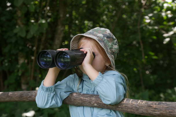 双眼鏡を通して自然を探検するかわいい少女. 屋外で遊んでいる子供. 子供旅行,アドベンチャー,バードウォッチングコンセプト. - 写真・画像