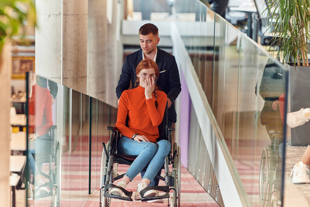 A company director assists his business colleague in a wheelchair, helping her navigate to their startup office, where they work alongside their diverse team of colleagues, emphasizing inclusivity and - Foto, Imagem