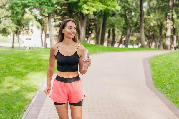 щаслива молода жінка вранці біжить з пляшкою води в парку. Спорт і здоровий спосіб життя. копіювання простору - Фото, зображення