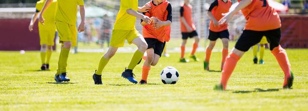 ヨーロッパのサッカーは若いチームの試合. サッカーの試合をする少年たち. ランニングとキックボールのジュニア競技. イエローとオレンジのキッズチームのトーナメントゲーム - 写真・画像