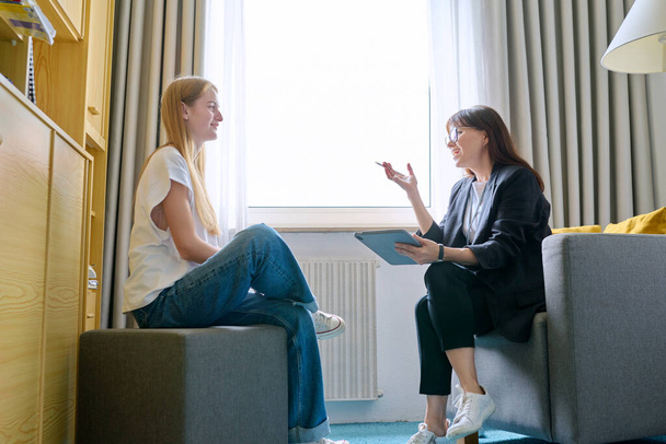 Young female at therapy meeting with psychotherapist. Session of teenage student girl, specialist psychologist with digital tablet talking to patient. Psychology, psychotherapy, treatment, youth - Fotó, kép