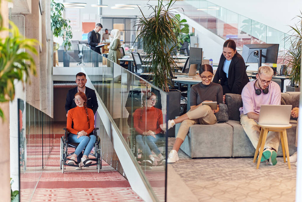 A company director assists his business colleague in a wheelchair, helping her navigate to their startup office, where they work alongside their diverse team of colleagues, emphasizing inclusivity and - Foto, Imagen