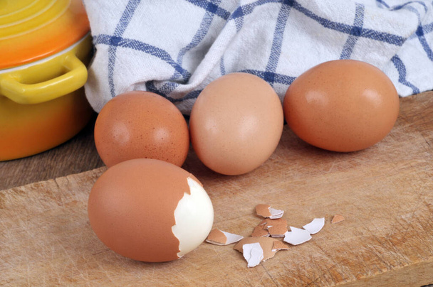 Huevo parcialmente pelado y cocido de cerca con huevos de pollo frescos en el fondo - Foto, imagen