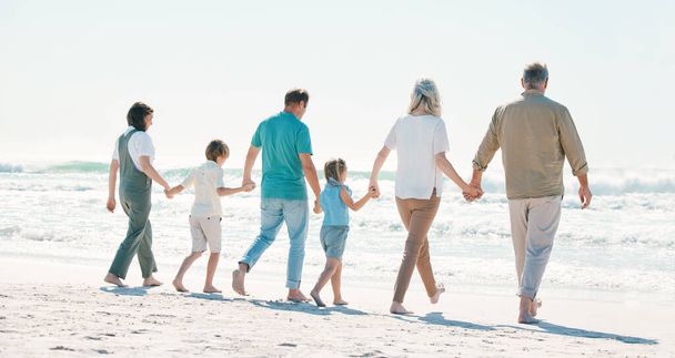 Love, travel and holding hands with big family on the beach for support, summer vacation or bonding. Freedom, health and relax with people walking on seaside holiday for adventure, trust or happiness. - Photo, Image