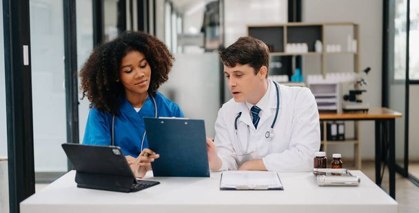 Focused mature male doctor and African female nurse discuss anamnesis together. Concentrated diverse medical professionals in hospital - Foto, imagen