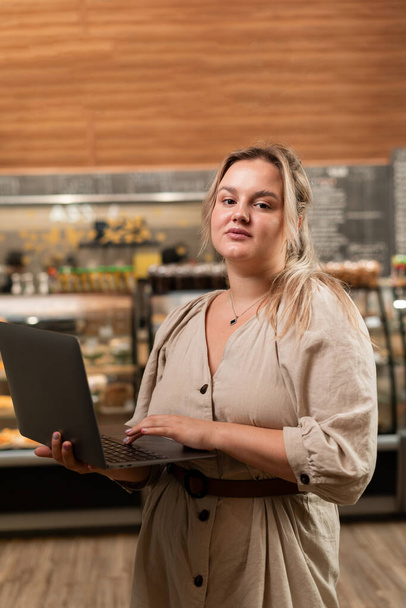 Businesswoman cafe owner with laptop in hands dressed dress standing near bar counter background caucasian female business person. Copy space - Foto, Imagen