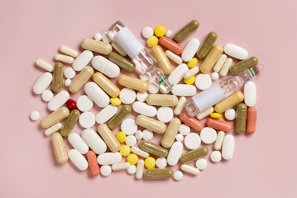 Mix of medical capsules and pills on light pink top view. Medicinal treatment. Taking dietary supplements and vitamins. Assorted pharmaceutical products - Photo, Image