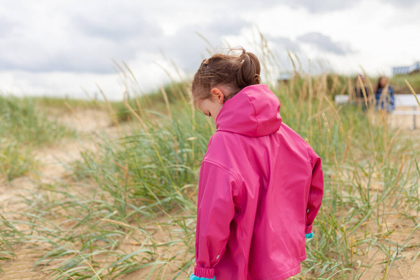 Rózsaszín esőkabátos kislány áll a homokdűnéken.. - Fotó, kép