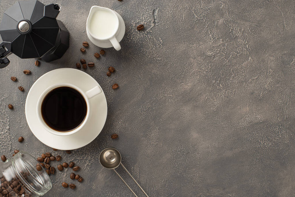 Barista's Haven: Caffè tostato in grani, tazzina espresso su piattino, barattolo di latte, misurino e bollitore visualizzati su elegante sfondo grunge scuro - Foto, immagini