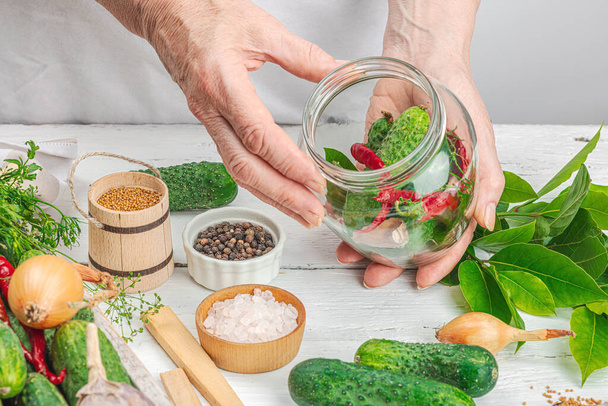 Preserved season vegetable concept. Harvest of cucumber, chili, greens, onion and garlic. Woman's hands prepare ingredients for canned food, home cooking process. Healthy recipes, copy space - Photo, Image
