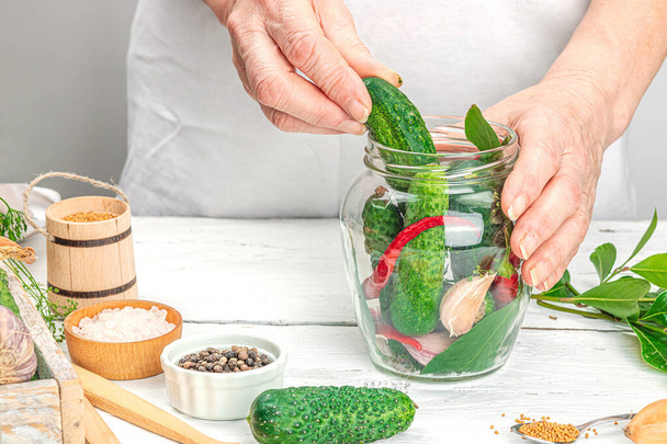 Preserved season vegetable concept. Harvest of cucumber, chili, greens, onion and garlic. Woman's hands prepare ingredients for canned food, home cooking process. Healthy recipes, copy space - Photo, Image