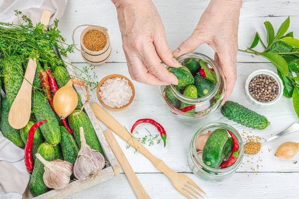 Preserved season vegetable concept. Harvest of cucumber, chili, greens, onion and garlic. Woman's hands prepare ingredients for canned food, home cooking process. Healthy recipes, top view - Photo, Image