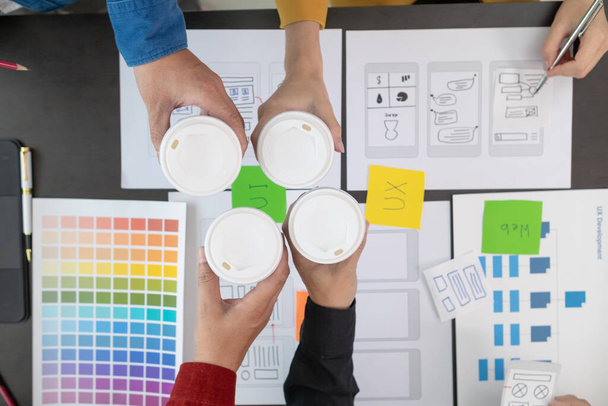 プログラマーとUI uxデザイナーは,別のラウンドを開始する前にコーヒーブーストを高めるためにブレイク中にデザインスタジオで一緒にホットコーヒーのカップを持っています. デザインチーム コーヒーブレイクコンセプト - 写真・画像