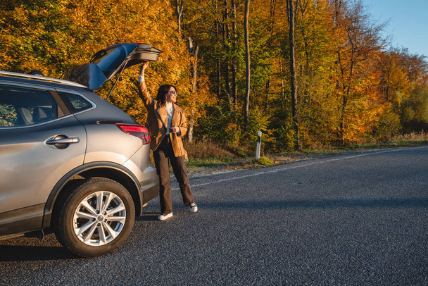 On forest background, smiling woman closes trunk of parked car - Photo, Image