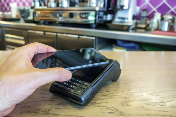 Клиент ресторана, использующий смартфон для оплаты в платежном терминале. Tpv. - Фото, изображение