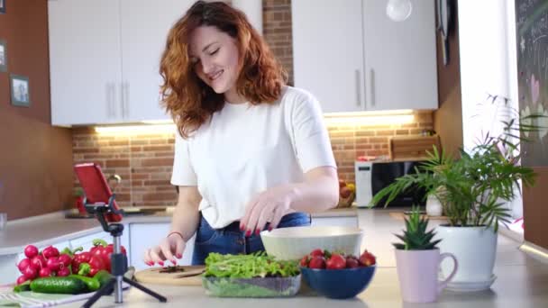 young caucasian woman at house kitchen tells recipe on camera while making salad. Online broadcast, author leads blog or course about cooking. - Footage, Video