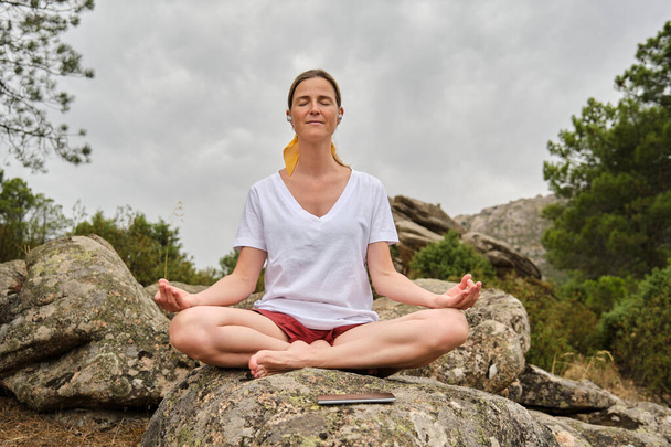 Frau meditiert in lockerer Pose während sie auf einem Felsen sitzt - Foto, Bild