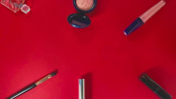 Flatlay met cosmetica rond de perimeter: parfums, oogschaduwen, lipgloss, make-up borstel, mascara en lippenstift op een felrode achtergrond. - Video