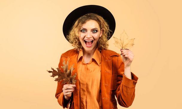 Smiling girl in fashionable wear with yellow leaf. Autumn fashion model in black hat. Autumn clothing for women. Happy woman in orange jacket with autumn leaves. Autumn time. Season sales. Discount - Photo, Image