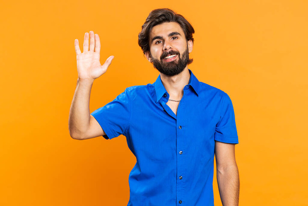 Come here, join us. Welcome. Attractive man showing inviting gesture with hands, ask to join, beckoning to coming, gesturing hello goodbye. Handsome middle eastern guy isolated on orange background - Photo, Image