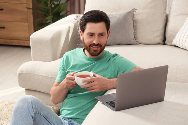Man with cup of tea using laptop at home - Фото, зображення