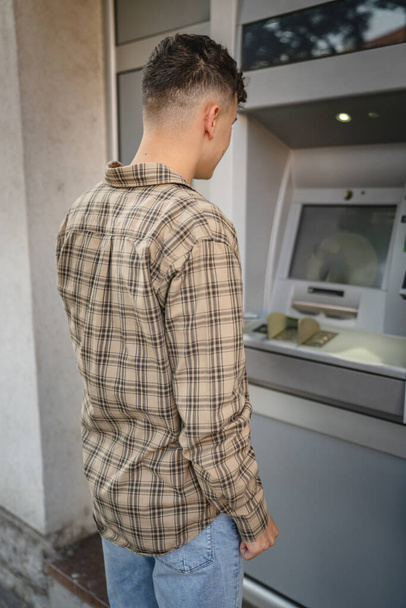 mężczyzna nastolatek student przy użyciu karty kredytowej i wypłaty gotówki w bankomacie - Zdjęcie, obraz