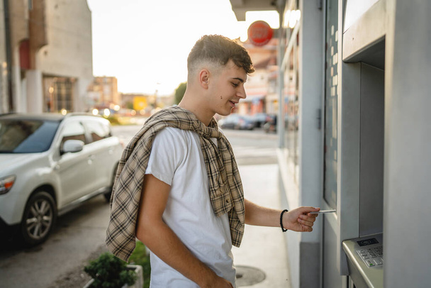 mężczyzna nastolatek student przy użyciu karty kredytowej i wypłaty gotówki w bankomacie - Zdjęcie, obraz