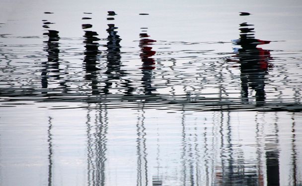 Reflection of people distorted on the water on the docks - Photo, Image